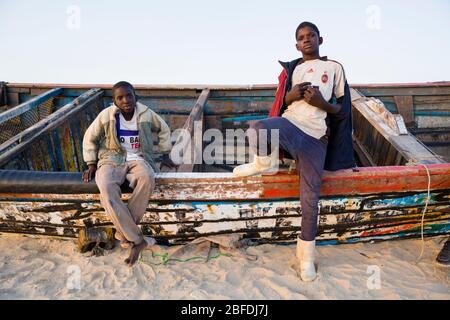 Junge Jungs und ein altes Fischerboot am Strand in Nouakchott, Mauretanien. Stockfoto