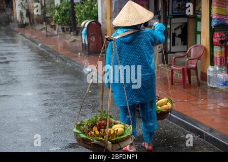 In Hoi an - Vietnam - am 2019. august - Frauen verkaufen Obst mit dem traditionellen Gewicht auf ihren Schultern - Straße der Altstadt Stockfoto