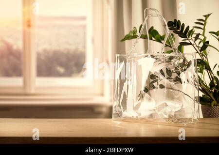 Holztisch mit Tasche und Kleidung und Kopierraum für Produkte. Schönes gemütliches und helles Zuhause. Hintergrund des Fensters mit natürlichem Licht. Stockfoto