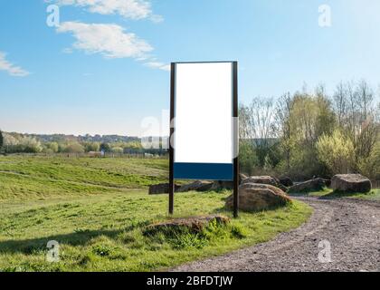 Leere/Mockup-Plakatwand im grünen Feld neben der Landstraße Gegen einen wolkigen blauen Himmel Stockfoto