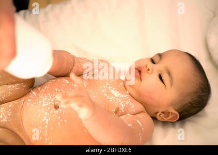 Eine Mutter drückt Babypulver auf die Brust und den Bauch ihres kleinen Babys Stockfoto