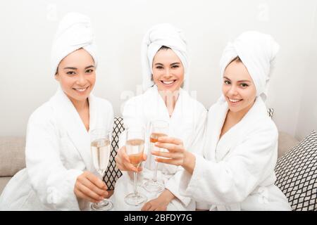 Frauen haben ein schönes Wochenende im Spa Resort. Drei schöne Frauen tragen Bademäntel und Handtücher auf dem Kopf Wein trinken und genießen Ruhe Stockfoto