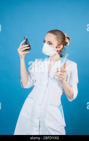 Schöne Frau Arzt in Schutzmaske gegen Coronavirus auf blauem Hintergrund Stockfoto