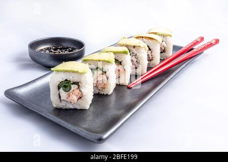 Sushi-Rolle mit Avocado-Wrap, gegrilltem Lachs, philadelphia-Käse und grünen Zwiebeln Schwarzer Behälter und rote Essstäbchen. Stockfoto