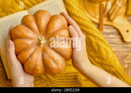 Herbstkonzept. Frau bewundert einen Kürbis mit einem Strickpullover und Buch Stockfoto
