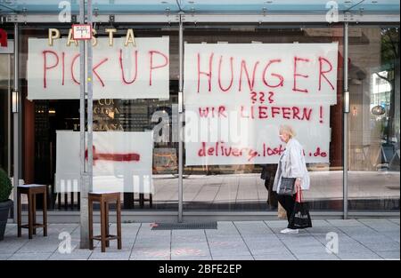 Stuttgart, Deutschland. April 2020. Eine Frau mit Gesichtsmaske geht an einem Restaurant vorbei, das mit großen Postern im Schaufenster einen Lieferservice und Take-away-Service anbietet. Quelle: Marijan Murat/dpa/Alamy Live News Stockfoto