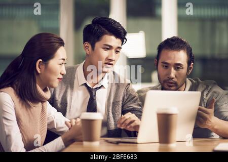 Team von drei jungen asiatischen Unternehmern, die sich im Büro treffen und eine Diskussion mit einem Laptop im Büro führen Stockfoto