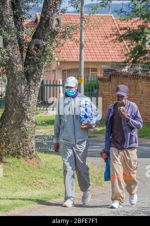 Alberton, Südafrika - unbekannte afrikanische Männer gehen nach Hause, nachdem sie während der nationalen Sperrzeit für wichtige Güter einkaufen Stockfoto