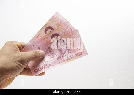 Eine mans-Hand hält drei 100 Banknoten auf weißem Hintergrund. Konzept Thai Baht Währung Banknote Stockfoto