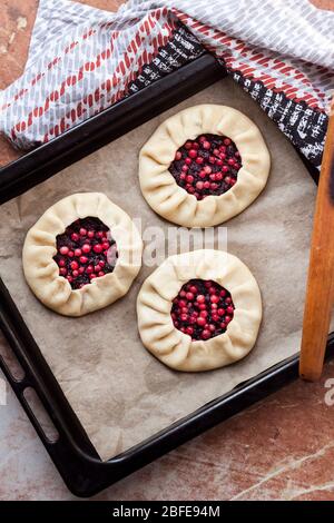 Hausmannskost. Süße Galette mit Holunderbeeren und Kuhbeeren auf Backblech zum Backen bereit. Flach liegend, Draufsicht Stockfoto