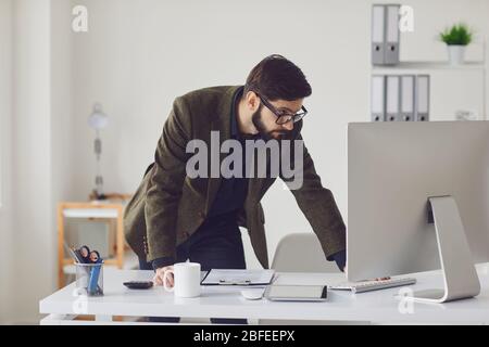 Geschäftsmann Arbeiter mit Bart in der Brille arbeitet hinter einem Computer für Stroh im Büro. Stockfoto