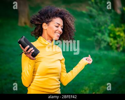 Moderne trendy afroamerikanischen Mädchen hören Musik von drahtlosen tragbaren speaker.Young schöne Frau genießen, tanzen im Park. Stockfoto