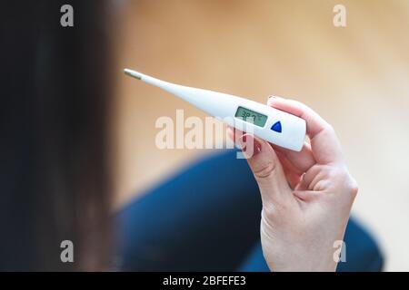 Selektiver Fokus einer Frau, die ein digitales Thermometer hält, das auf über 38 Grad Fieber hinweist. Kranke und besorgte Frau mit Fieber und Krankheit Stockfoto