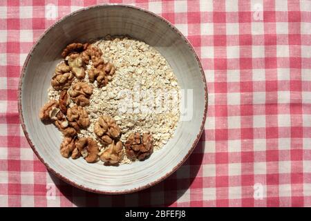 Haferflocken und Walnüsse in Vintage-Schüssel auf einer rot-weiß karierten Stoffserviette. Gesunde hausgemachte Haferflocken zum Frühstück. Tageslicht. Stockfoto