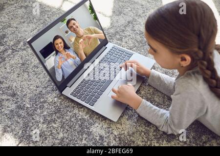 Online-Chat mit der Familie. Online-Video-Chat kleine Tochter begrüßt ihre Eltern entfernt auf dem Boden bei home.Communication von Menschen mit liegen Stockfoto