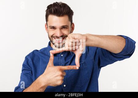 Porträt eines jungen Geschäftsmannes, der einen Rahmen aus seinen Fingern formt und durch ihn zur Kamera lächelt, auf weiß. Stockfoto