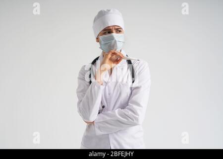 Traurig überrascht Arzt trägt medizinische Gesichtsmaske hält medizinische Thermometer über weißem Hintergrund Stockfoto
