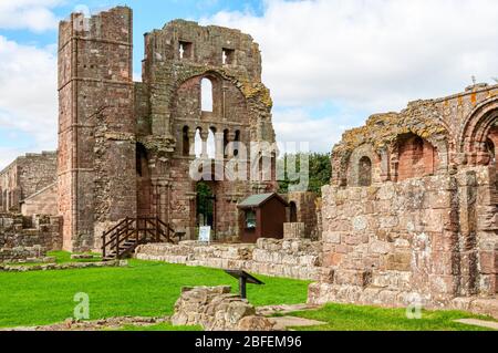 Das imposante befestigte Westtor der dunkelroten Sandsteinkirche des Lundisfarne Priory mit einem noch stehenden Turm und Armbrust-Schleifen sichtbar Stockfoto