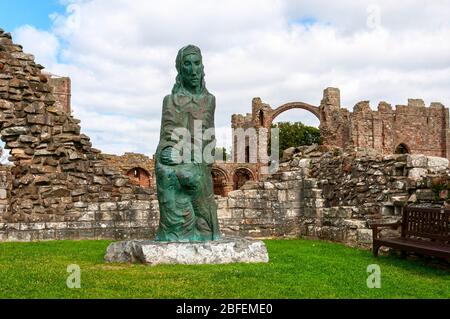 Eine Bronzestatue des hl. Cuthbert, die von Fenwick Lawson geformt wurde, befindet sich im äußeren Hof des Priorats von Lindisfarne mit dem Regenbogenbogen auf der Rückseite Stockfoto