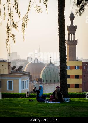 Al Azhar Park, Kairo, Ägypten, Oktober 2019, drei Mädchen sitzen auf einer Decke im Park mit der Skyline von Kairo im Hintergrund Stockfoto