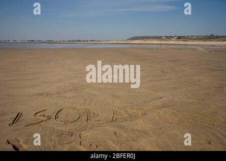 Das Wort Isolation schrieb sich in den frühen Tagen der pandemischen Sperrung auf dem Sand des Newton Beach jenseits der Black Rocks ein Stockfoto