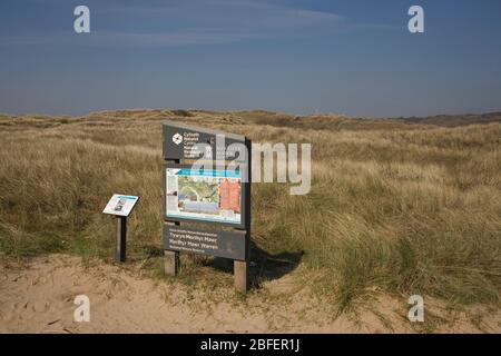 Grasbedeckte Sanddünen neben dem Hauptschild des Merthyr Mawr National Nature Reserve an sonnigen Frühlingstag Stockfoto