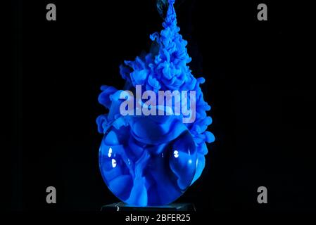 Glaskugel mit blauer Farbe spritzt unter Wasser und auf einem schwarzen Backgorund. Stockfoto