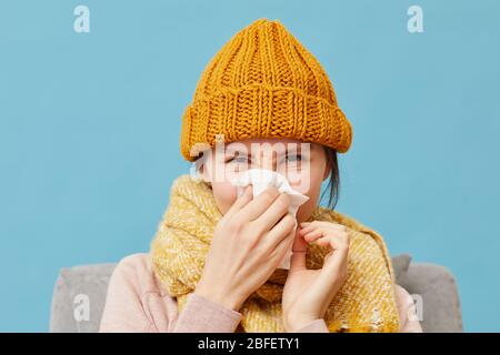 Portrait der jungen Frau in Wollmütze und Schal hat eine laufende Nase isoliert auf blauem Hintergrund Stockfoto