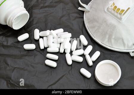 Verstreute Pillen und ein Atemschutzgerät auf schwarzem Hintergrund. Virenschutz. COVID-19. Stockfoto