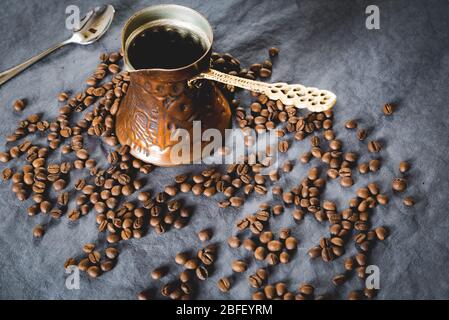 Flacher Einlage von dunklen Kaffeebohnen auf dunklem Hintergrund mit türkischer Kaffeekanne, Kupfer oder Zezve verstreut. Traditionelle türkische Kaffeebrauerei Stockfoto