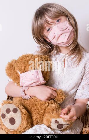 Mädchen mit selbstgemachten covid 19 Schutzmaske mit ihrem Teddybär Stockfoto