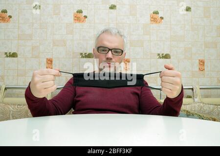 COVID-19. Bleiben Sie zu Hause und distanzieren Sie sich. Ein junger Mann in einer schwarzen medizinischen Maske sitzt zu Hause. Stockfoto