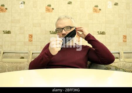 COVID-19. Bleiben Sie zu Hause und distanzieren Sie sich. Ein junger Mann in einer schwarzen medizinischen Maske sitzt zu Hause. Stockfoto