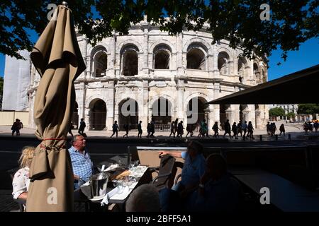 Menschen sitzen auf Café-Esplanade vor der Arena von Nîmes römischen Amphitheater in Nimes, Frankreich, Europa Stockfoto