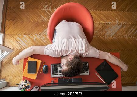 Der Mann schläft auf einer Tastatur, er arbeitet ferngesteuert zu Hause auf einem Computer. Konzept der Selbstisolierung während einer Pandemie. Moderner Lebensstil. Stockfoto