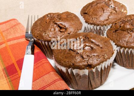 Hausgemachte Schokolade Zimt Muffins in Jumbo-Größe Papier Liner auf einem weißen Teller mit einem Burlap Stoff Hintergrund. Stockfoto