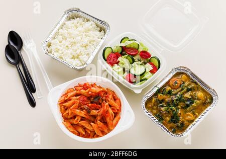 Essen zum Mitnehmen in Einwegbehältern: Reis, Gemüsecurry, italienische Pasta mit Tomatensauce und frischer gesunder Salat. Stockfoto