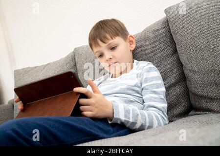 Junge, die vor dem Tablet-pc denken, suchen. Fernunterricht Online-Bildung. Niedlichen kaukasischen Jungen tun Hausaufgaben zu Hause während Quarantäne von Stockfoto