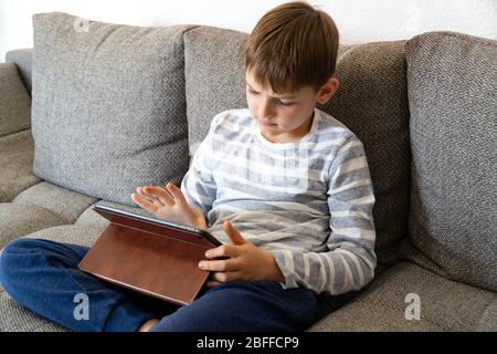 Junge, die vor dem Tablet-pc denken, suchen. Fernunterricht Online-Bildung. Niedlichen kaukasischen Jungen tun Hausaufgaben zu Hause während Quarantäne von Stockfoto