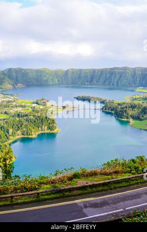 Wundervolle Aussicht auf die Seen Sete Cidades, fotografiert vom Aussichtspunkt Vista do Rei auf der Insel San Miguel, den Azoren, Portugal. Blauer Vulkansee umgeben von grünem Wald. Straße im Vordergrund. Stockfoto