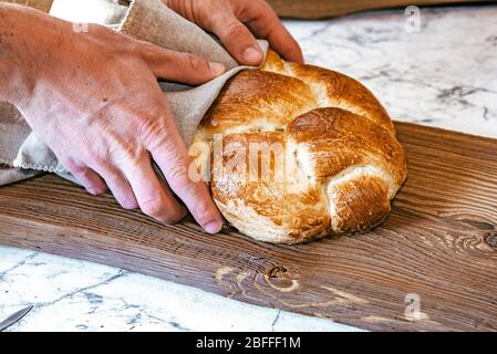 Hausgemachtes jüdisches traditionelles Challah-Brot auf rustikalem Holzbrett. Blick von oben auf warme frisch gebackene Challah in den Händen. Stockfoto