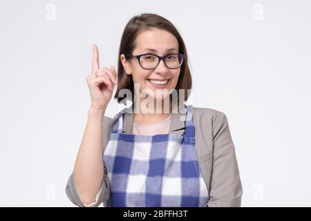 Reife kaukasische Frau in Anzug und Schürze hält Zeigefinger bis geben Ratschläge. Geschäftsfrau, die Erfolg an Haus-Aufgaben auch hat. Stockfoto