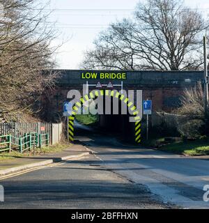 Fernansicht eines einspurigen Tunnels mit gelben und schwarzen Warnstreifen und Schriftzug, der Low Bridge angibt. Es gibt auch blattlose Bäume si Stockfoto