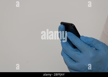 Hände geschützt mit Nitril-Handschuhen, die ein Mobiltelefon halten Stockfoto