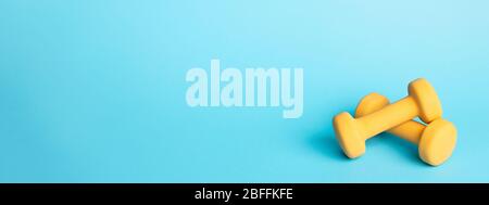 Banner mit zwei gelben Kurzhanteln auf blauem Hintergrund mit Kopierfläche. Sport und Fitness. Stockfoto