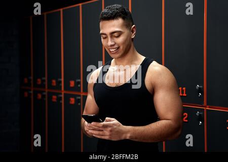 Junger Erwachsener Sportler lächelnd, mit modernen Smartphone Stockfoto