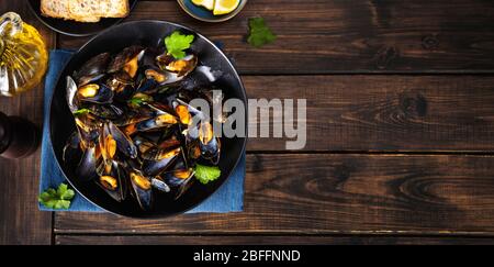 Draufsicht auf gedünstete Muscheln auf einer schwarzen Platte Rustikaler Holzhintergrund Stockfoto