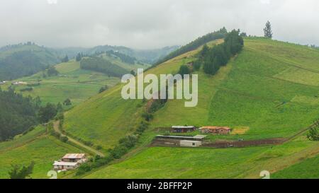 Ecuadorianische Gebirgslandschaft mit Bergen mit grünen Feldern, Bäumen und kleinen Häusern an einem bewölkten Tag Stockfoto