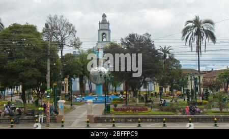 Cayambe, Pichincha / Ecuador - Februar 24 2020: Menschen sitzen im zentralen Park der Stadt mit der Matriz-Kirche im Hintergrund Stockfoto