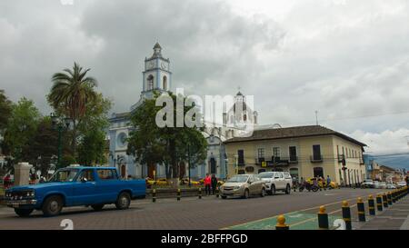 Cayambe, Pichincha / Ecuador - Februar 24 2020: Menschen, die in der Nähe des zentralen Parks der Stadt mit der Matriz-Kirche im Hintergrund zu Fuß Stockfoto